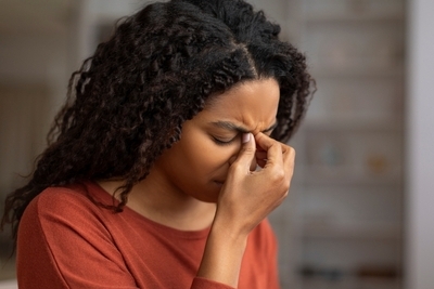 Woman-suffering-in-Sinusitis-condition Black-woman-holding-her-nose-feeling-uncomfortable-in-orange-shirt.
