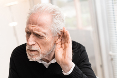 Elderly man cupping his ear, struggling to hear clearly